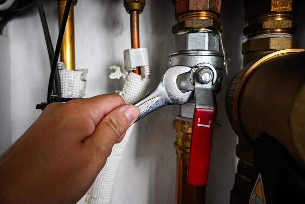 A hand expertly uses a wrench to tighten a fitting on a metal pipe system, featuring copper parts and a red-handled valve. Both insulated and uninsulated sections are visible, showcasing the precision of plumbing services in Cook County, IL.