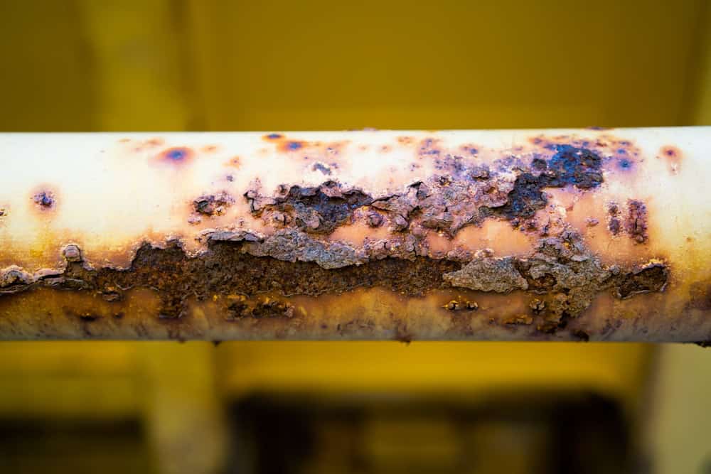 A close-up of a yellow metal pipe with extensive brown rust and corrosion, showing peeling and flaking areas—typical issues a plumber in Chicago & Cook County, IL might address—set against a blurred yellow background.