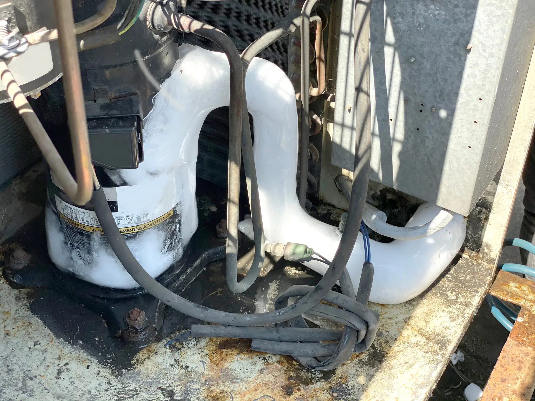Close-up of an HVAC compressor unit with frost and ice buildup on the pipes and surrounding components, indicating a possible malfunction or issue with the air conditioning system.