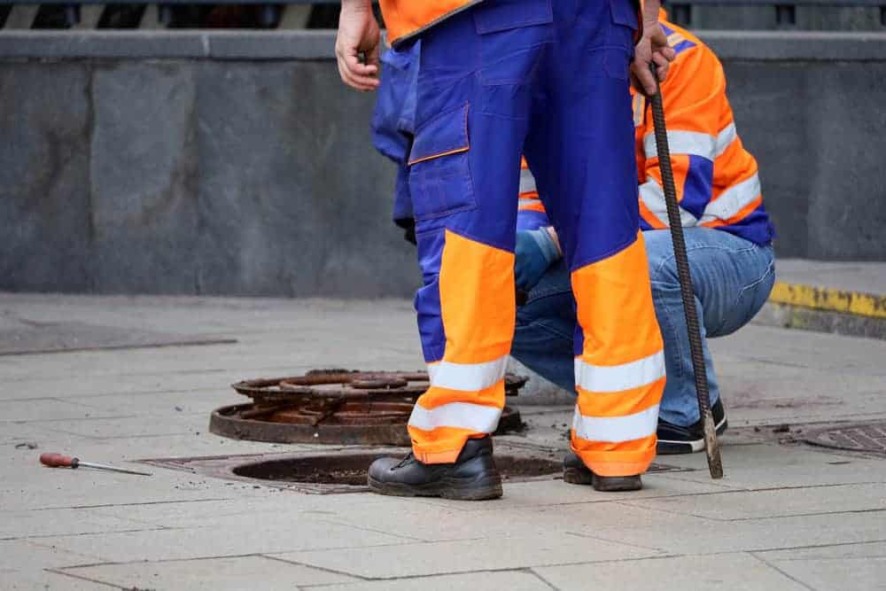 Two workers in safety vests stand over an open sewer hatch on a Chicago street, performing maintenance in Cook County, IL