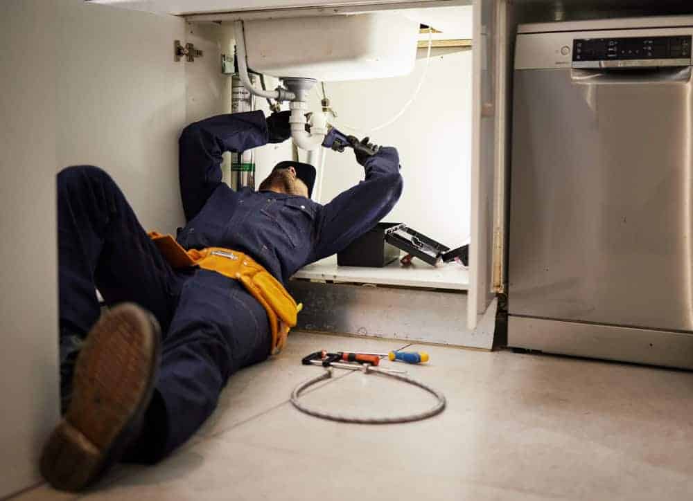 Professional plumber in blue uniform installs pipes on a kitchen floor during a modern home renovation in Chicago