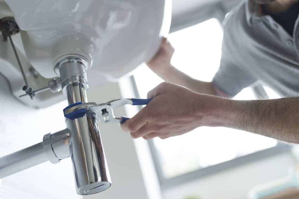 A professional plumber in Chicago carefully repairs a leaking bathroom sink using a wrench to tighten a silver pipe