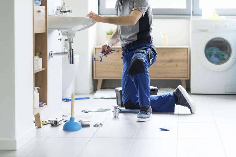 Professional plumber in uniform repairing a ceramic bathroom sink drain in a Chicago, Illinois home