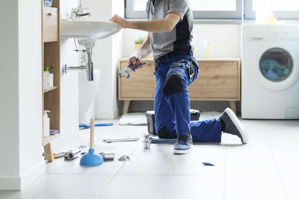 Professional plumber in uniform repairing a bathroom sink drain in Chicago, Cook County, IL; closeup of hands and tools