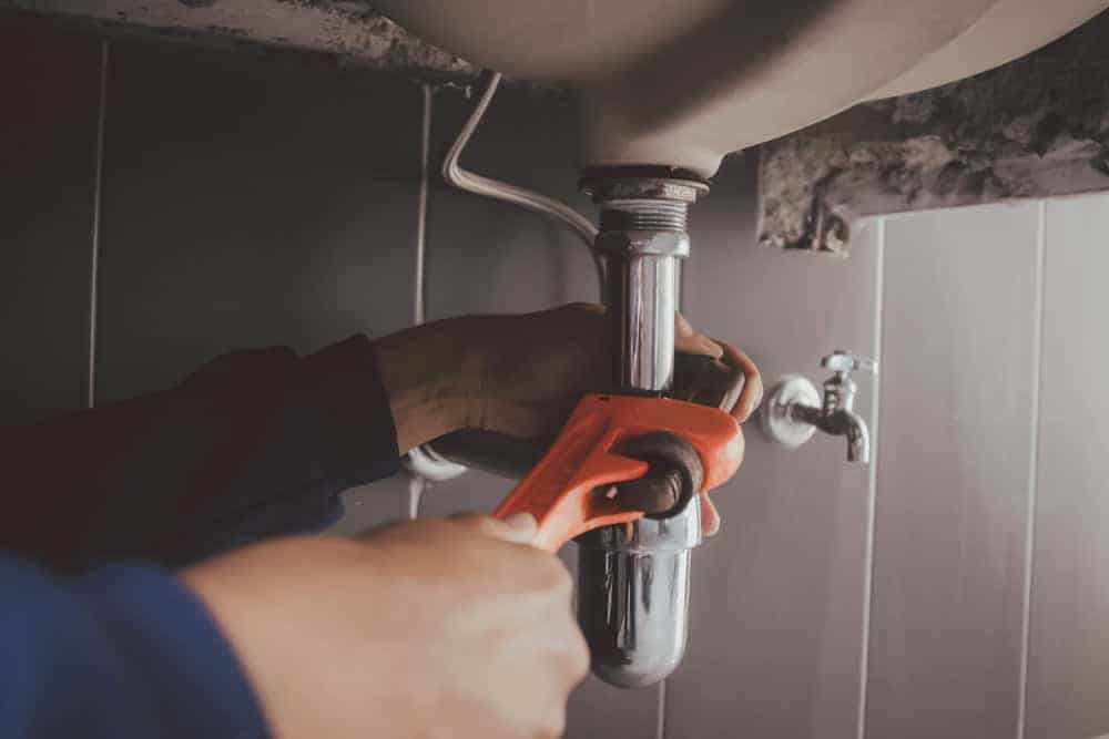 A professional plumber repairs a pipe under a bathroom sink in Chicago, Illinois, using a wrench to fix a leak